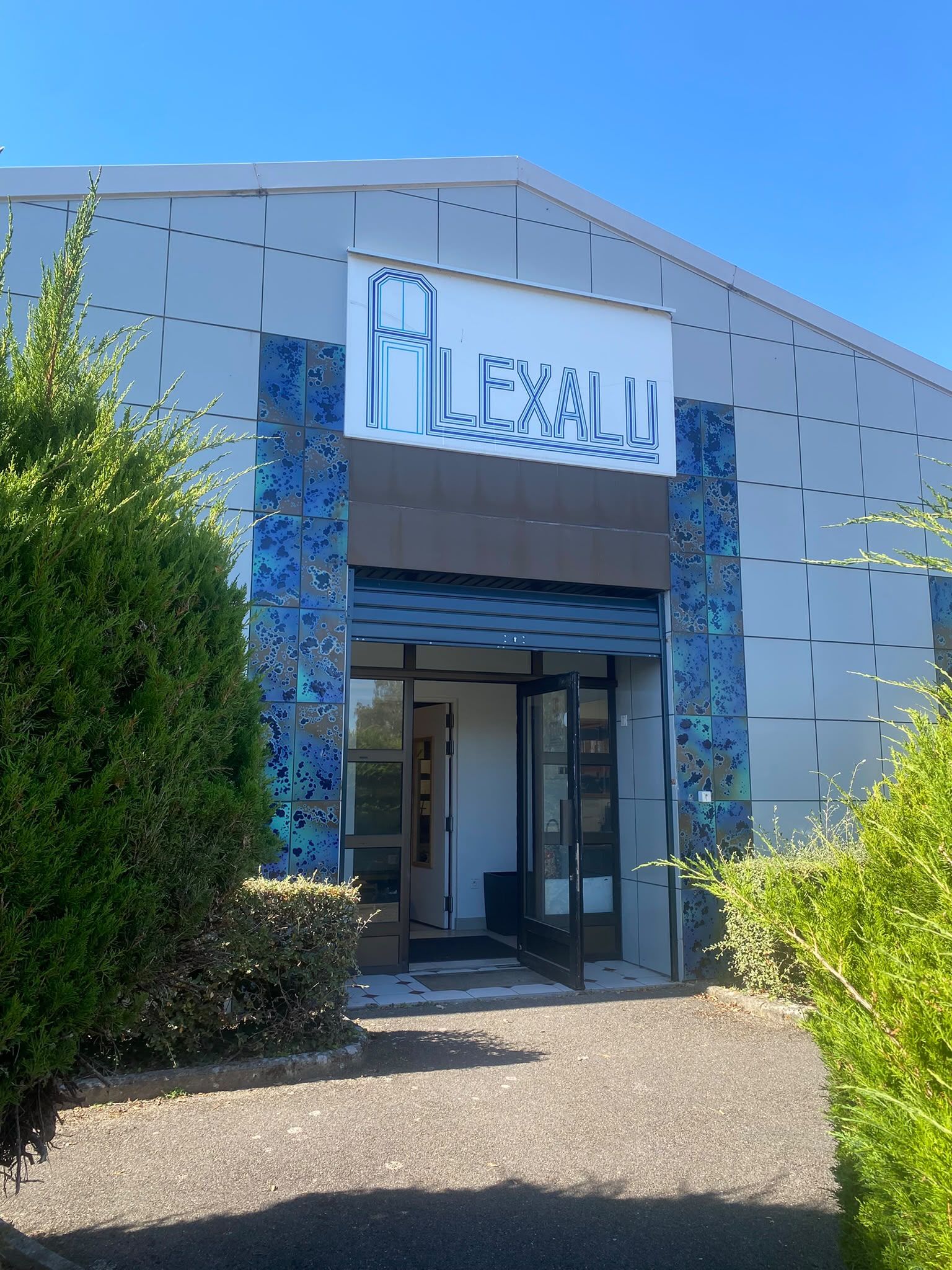 Entrée du bâtiment AlexAlu à Chaumont-en-Vexin, enseigne ALEXALU au-dessus de la porte vitrée