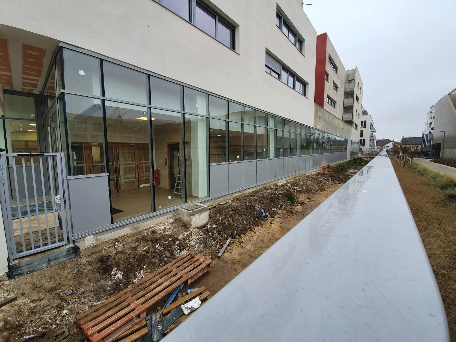 Façade vitrée aluminium en rez-de-chaussée d'un immeuble neuf, chantier en cours de finition le long d'une allée